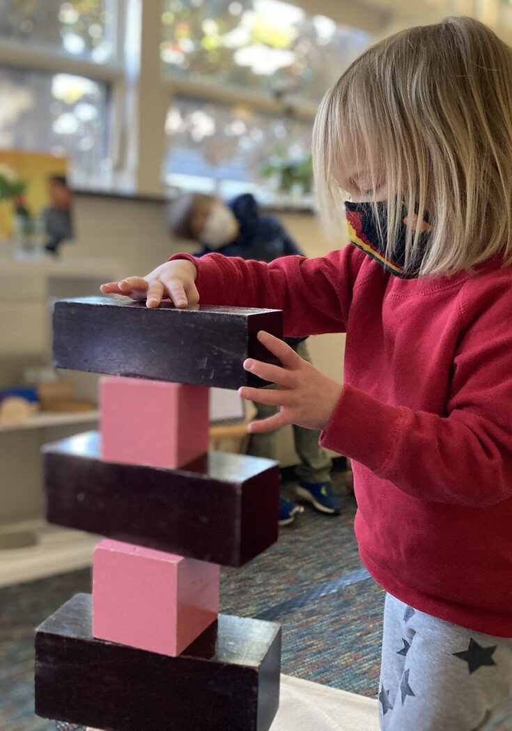 primary student building a tower from Montessori materials.